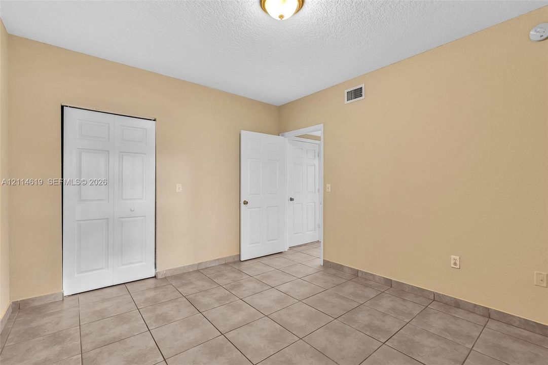 Neutral-toned room featuring large-format square tile flooring, six-panel interior doors, a double-door reach-in closet, and a central ceiling-mounted light fixture
