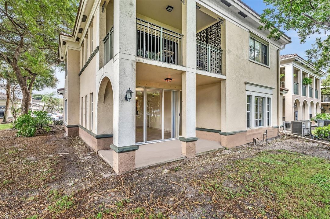 Multi-story stucco exterior featuring a covered patio, a second-level balcony with decorative iron railings, arched architectural detailing, and large glass sliding doors