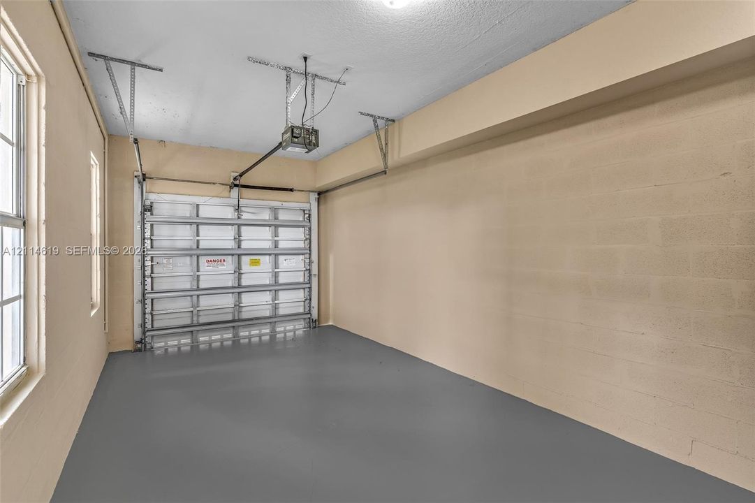 Garage space featuring finished epoxy flooring, concrete block walls, a sectional overhead garage door, and windows providing natural light