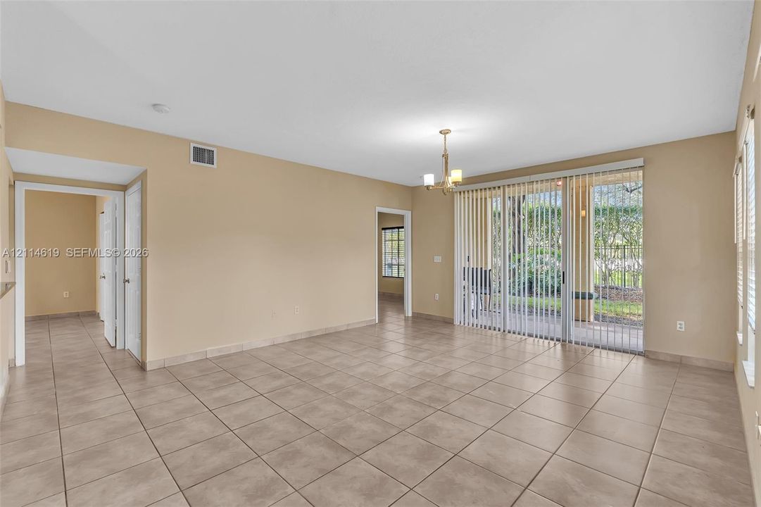 Spacious room featuring neutral ceramic tile flooring, a multi-arm chandelier, and sliding glass doors with vertical blinds