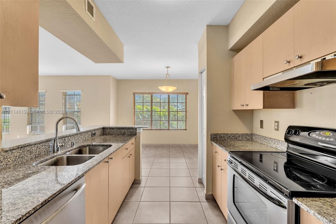 Kitchen featuring flat-panel cabinetry, stone countertops, double basin stainless steel sink, stainless steel range with overhead hood, and ceramic tile flooring