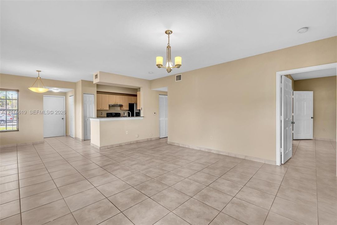 Open-concept interior featuring large-format ceramic tile flooring, neutral wall tones, multi-arm chandelier lighting, and a kitchen with wood-finish cabinetry