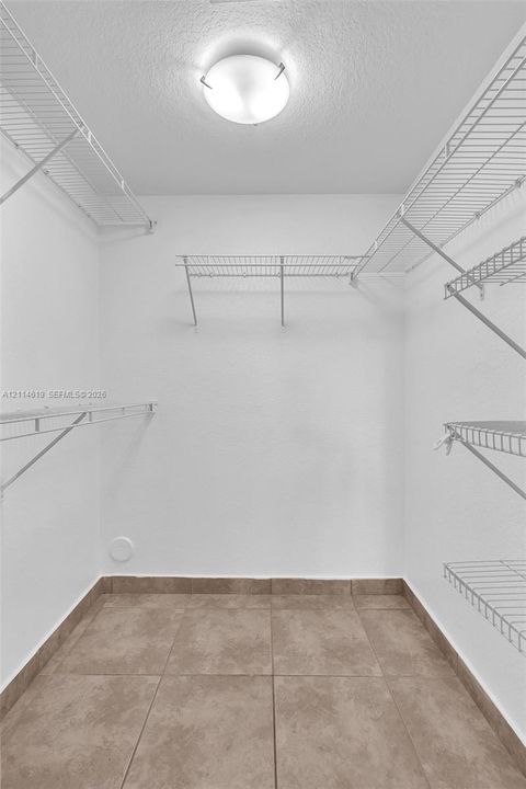 Walk-in closet featuring large-format neutral floor tiling, multiple levels of white wire shelving, and a dome-style flush-mount ceiling light