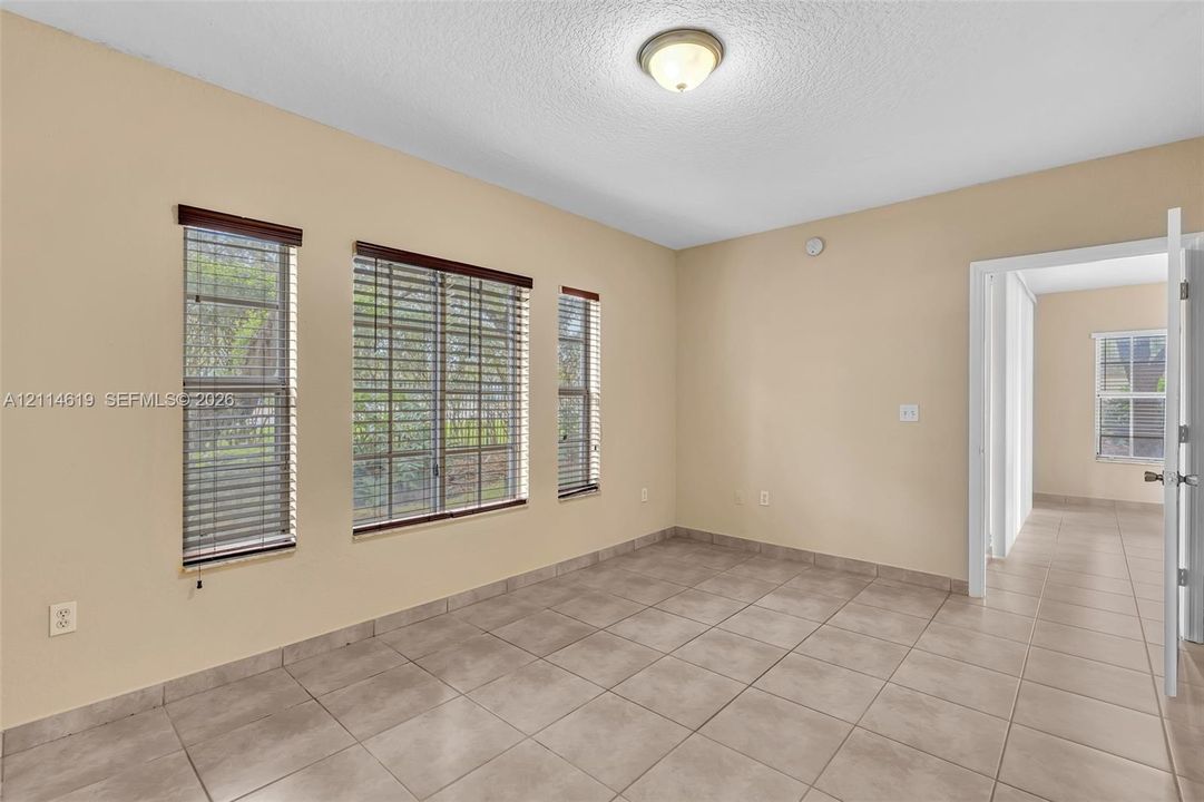 Neutral-toned interior featuring large-format ceramic tile flooring, triple-window configuration with horizontal blinds, and a flush-mount ceiling light fixture