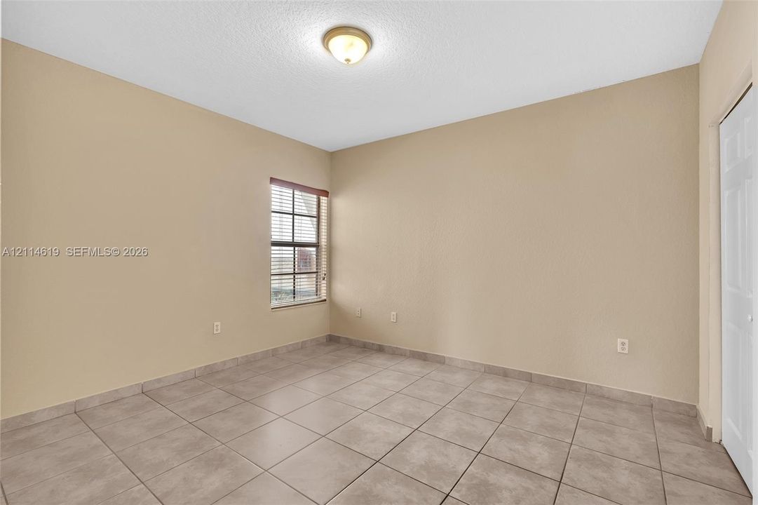 Neutral-toned interior space featuring ceramic tile flooring, a multi-pane window with installed blinds, a ceiling-mounted light fixture, and a white paneled closet door