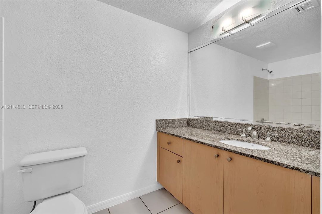 Bathroom featuring a stone-composite countertop, light wood cabinetry, a full-width wall mirror, and a tiled shower enclosure