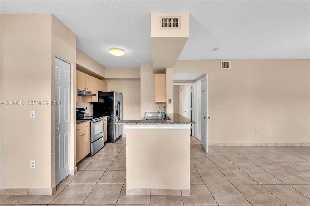 Kitchen featuring a stone-look countertop breakfast bar, wood-finish cabinetry, stainless steel range and refrigerator, and ceramic tile flooring