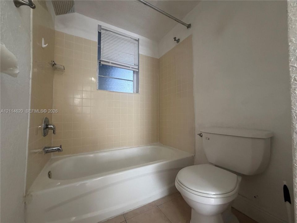 Bathroom featuring a porcelain tub, beige square-tile wall surround, chrome plumbing fixtures, and a window with integrated blinds