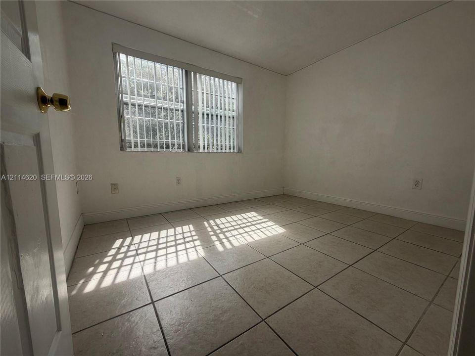 Room featuring neutral-toned tile flooring, white-painted walls, and a window with security bars