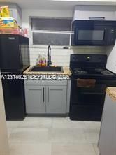 Kitchen featuring gray shaker-style cabinetry, a stone-finish countertop, white subway tile backsplash, a deep-basin sink with a matte black faucet, and matching black appliances