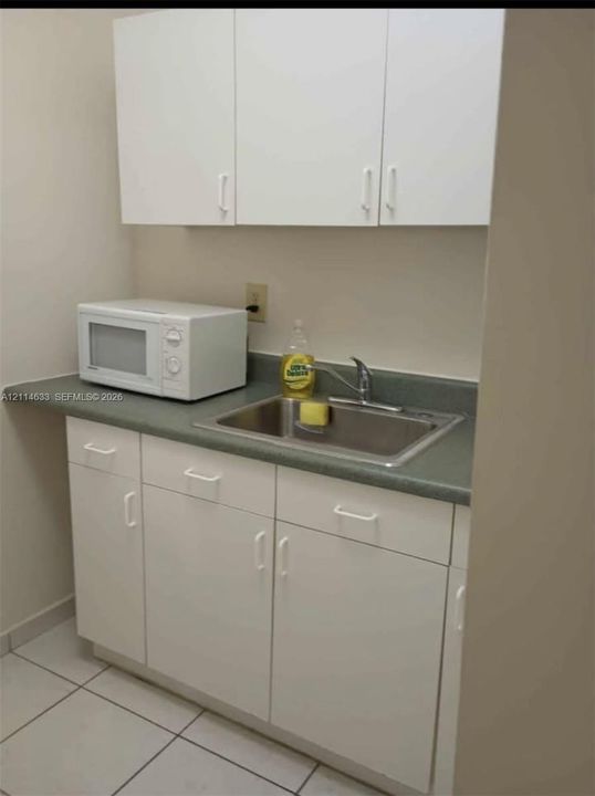 Kitchenette featuring white cabinetry, neutral-toned solid surface countertop, stainless steel sink, and chrome finish faucet