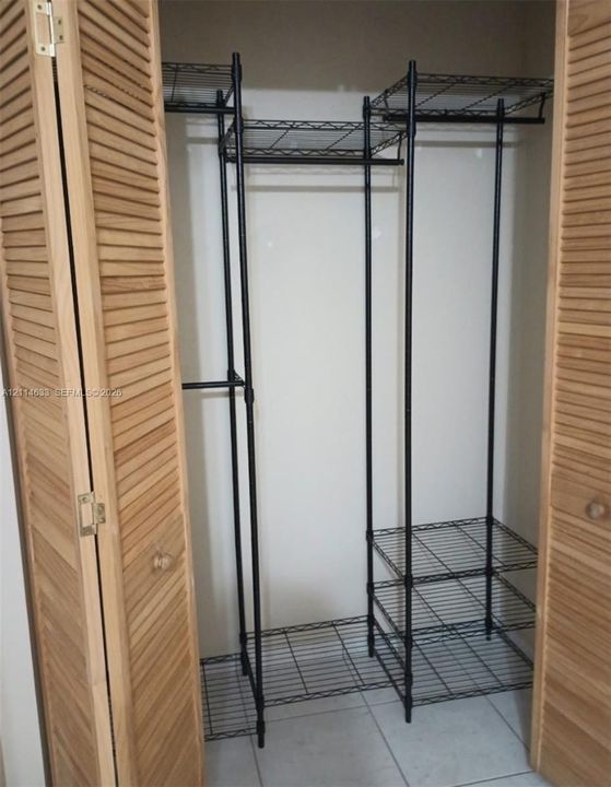 Closet featuring light-tone wood louvered doors, black metal wire shelving, and overhead storage tiers