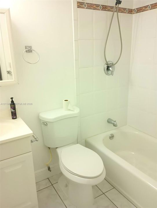 Bathroom featuring a vanity with an integrated basin, white tile surround, tub-shower combination, and tiled flooring