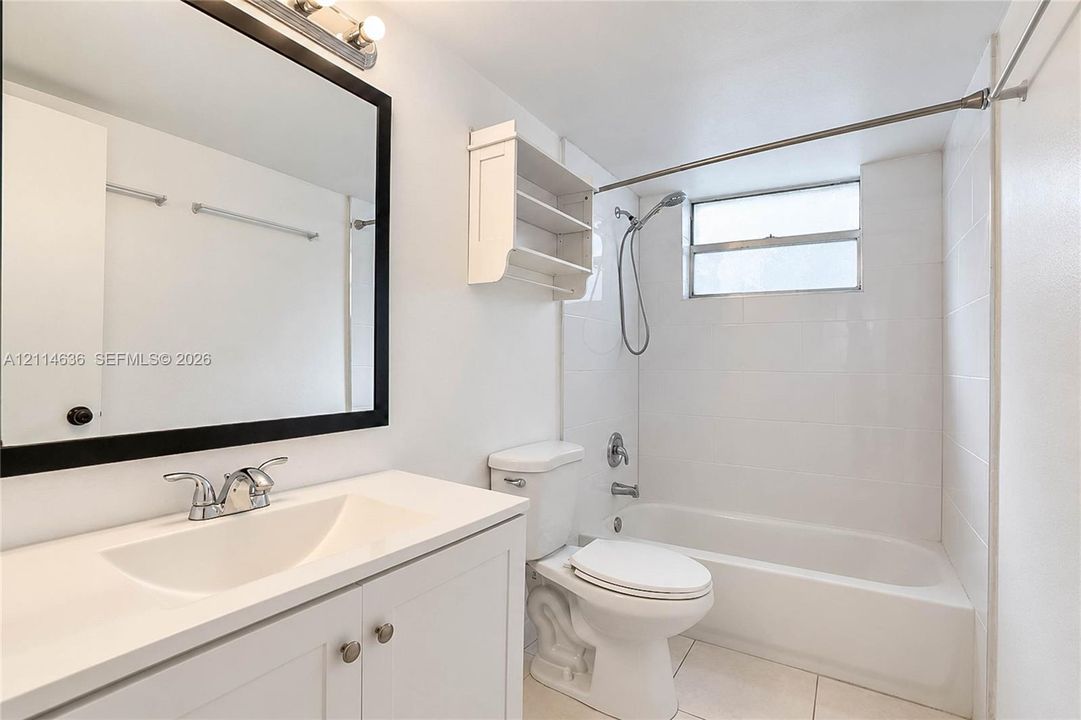 Bathroom featuring a vanity with an integrated sink, framed mirror, wall-mounted shelving, tiled tub surround, and a handheld shower fixture