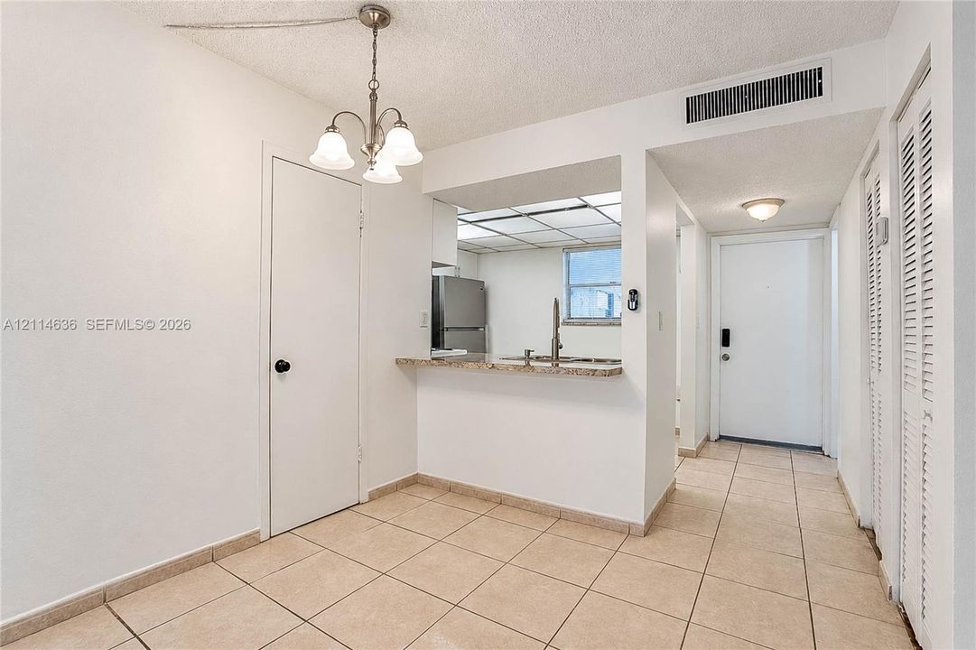 Ceramic tile flooring, three-light chandelier, stone-surface breakfast bar, stainless steel refrigerator, and louvered bi-fold closet doors