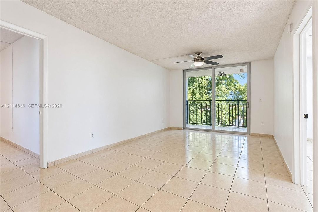Open-concept interior featuring neutral tile flooring, ceiling fan with integrated lighting, and glass sliding doors providing access to a private balcony with metal railing