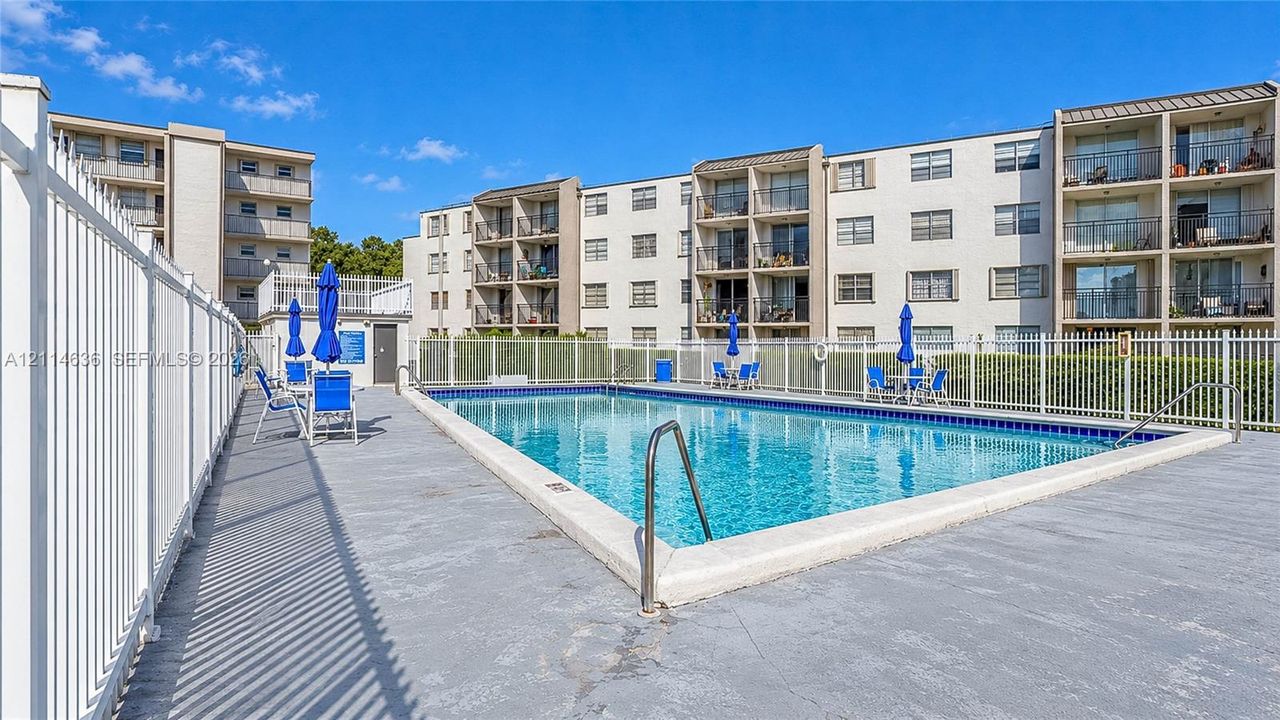 In-ground swimming pool featuring a concrete deck, white perimeter fencing, and metal handrails