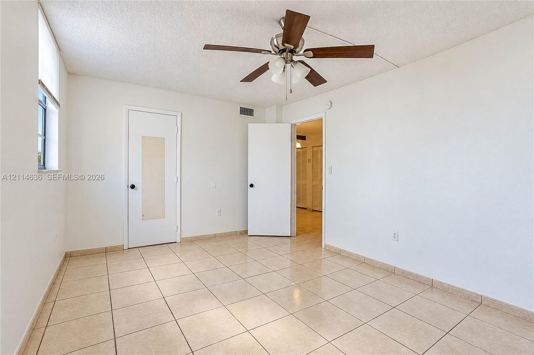 Interior space featuring neutral tile flooring, a multi-blade ceiling fan with integrated lighting, and a single-panel door with a central translucent inlay