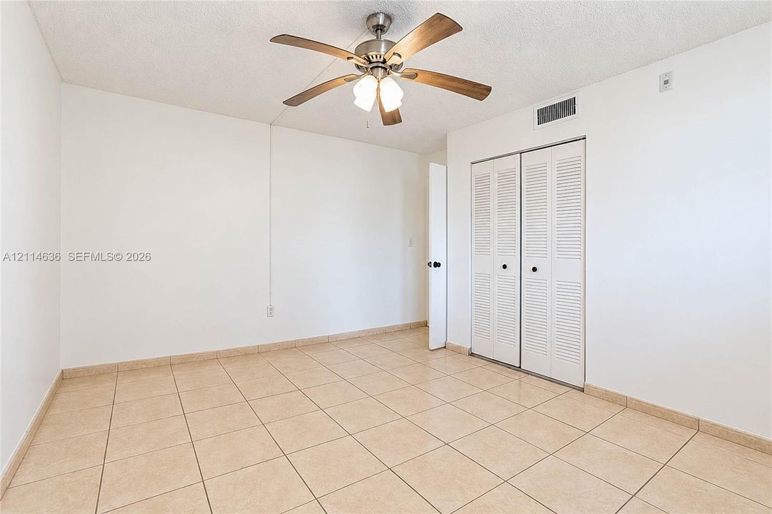 Room featuring neutral ceramic tile flooring, a brushed nickel ceiling fan with integrated lighting, and a closet with white louvered bi-fold doors