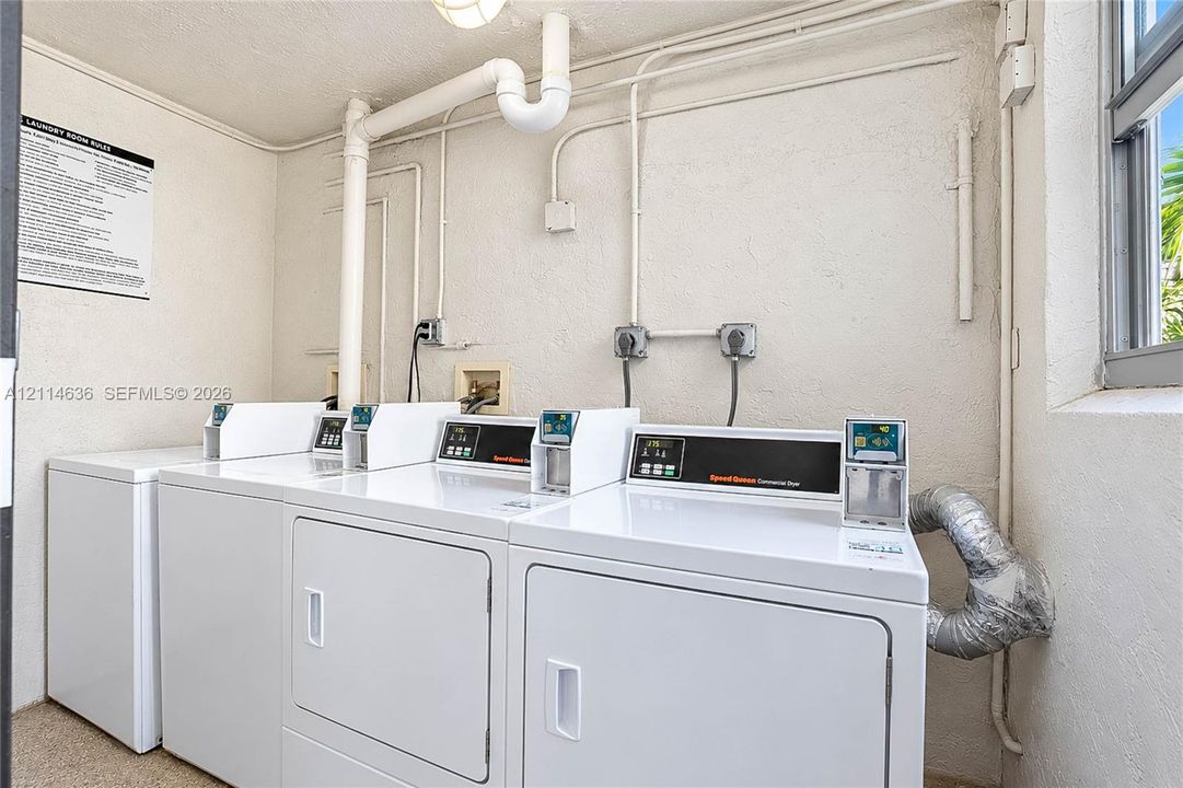 Laundry facility equipped with multiple commercial-grade dryers, wall-mounted electrical outlets, and a window