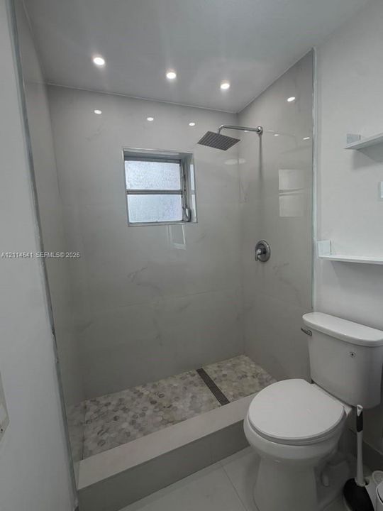 Walk-in shower featuring large-format wall tiling, stone pebble flooring, rainfall showerhead, and integrated recessed lighting