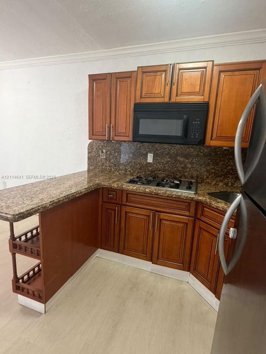 Kitchen featuring wood cabinetry, stone-surface countertops, integrated gas cooktop, built-in microwave, and open shelving end-cap