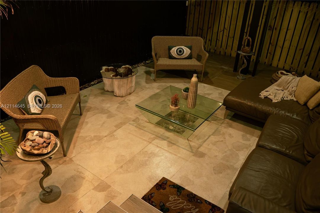 Outdoor patio featuring large-format light-toned stone tile flooring, vertical wood-plank perimeter fencing, and a dark privacy wall
