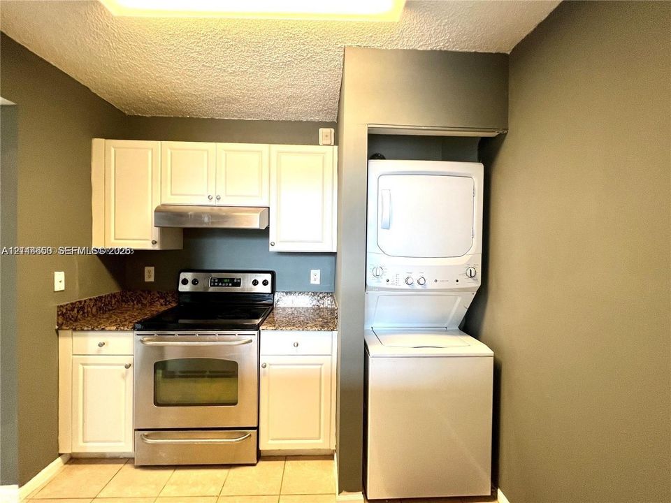 Kitchen featuring white cabinetry, stone-finish countertops, stainless steel range with integrated hood, and a stacked washer and dryer unit