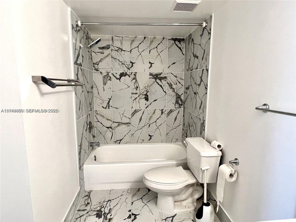 Full-height wall tiling with a high-contrast vein pattern, built-in bathtub, and chrome-finish fixtures