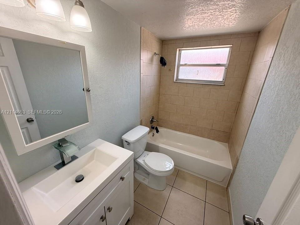 Bathroom featuring a white vanity with a rectangular sink, waterfall faucet, framed wall-mounted mirror, ceramic tile flooring, and a tiled tub surround