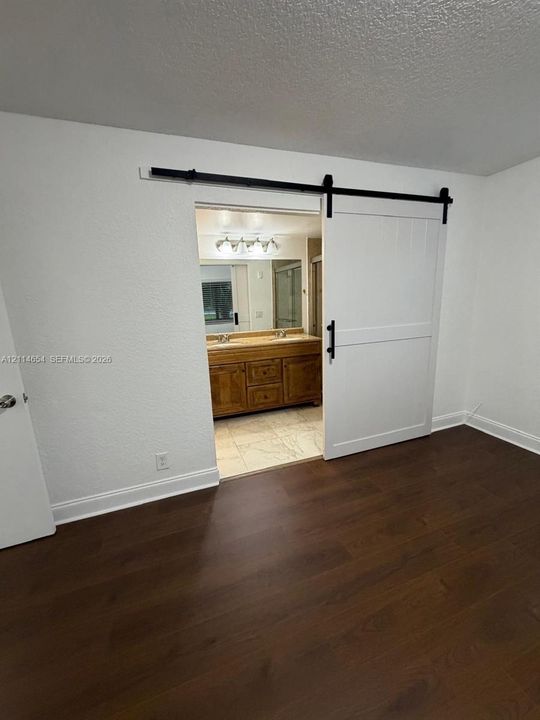 Wood-finish flooring featuring a white sliding barn door on a black metal track, with an attached bathroom vanity including dual sinks, cabinet storage, and four-light vanity fixture