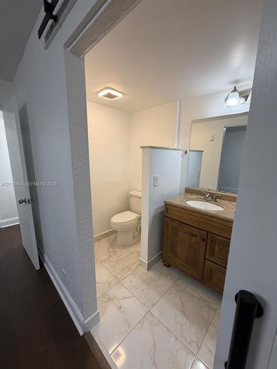 Bathroom featuring large-format stone-finish tile flooring, wood-finish cabinetry, an integrated vanity countertop with an oval basin, and a wall-mounted vanity mirror with a single-light fixture