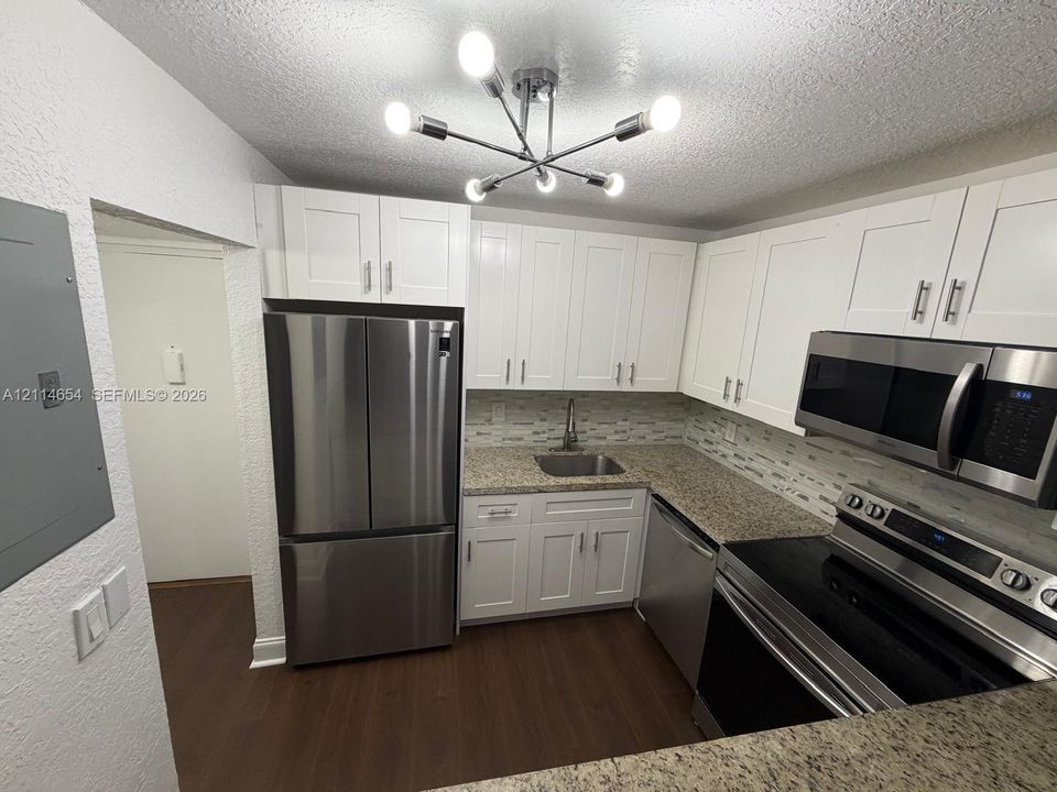 Kitchen featuring white shaker-style cabinetry, stone-finish countertops, stainless steel appliances, multi-toned tile backsplash, and a contemporary multi-arm light fixture
