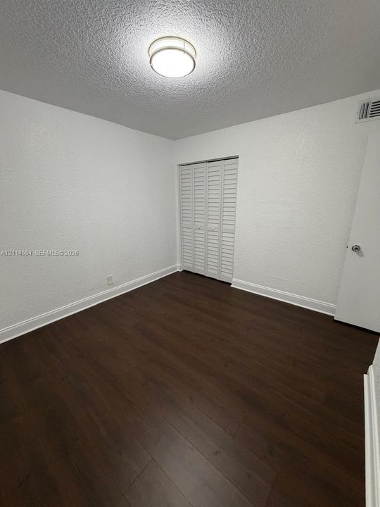 Room featuring dark wood-finish flooring, white textured walls, and a bi-fold louvered closet door