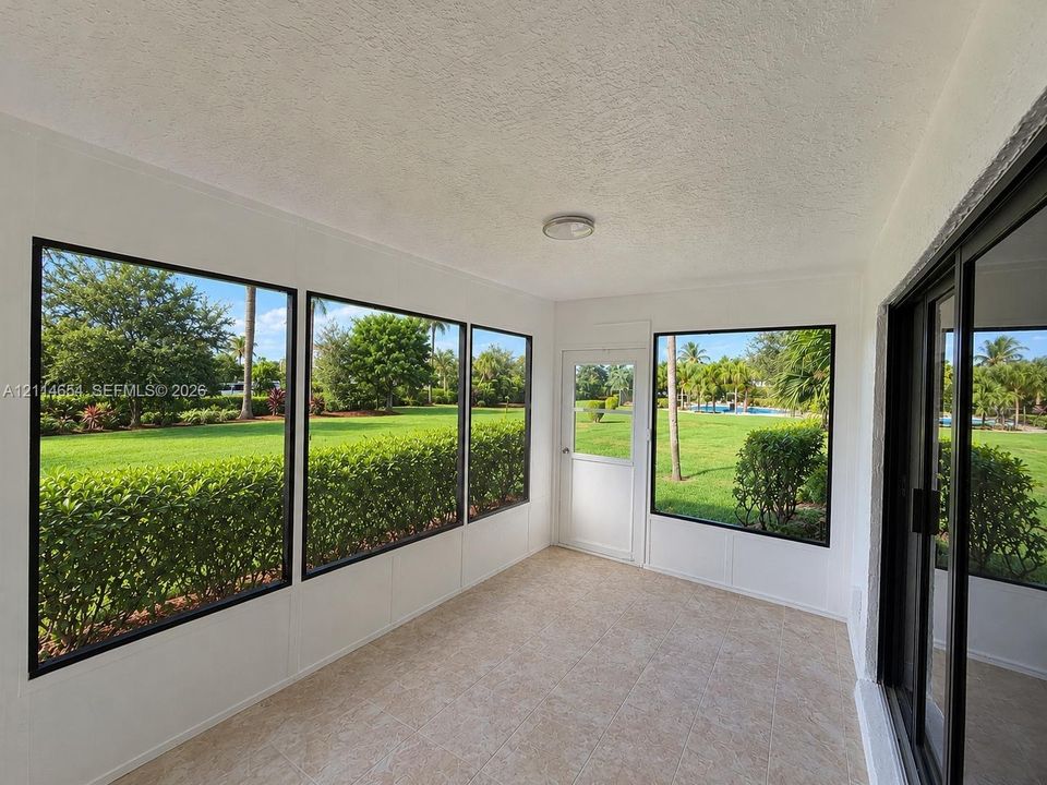 Enclosed sunroom featuring expansive windows with black frames, tile flooring, and a glass-paneled entry door