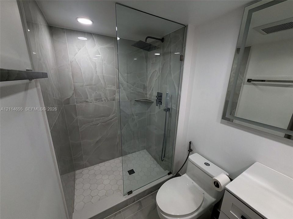 Walk-in shower featuring large-format stone-finish tile surround, frameless glass enclosure, rainfall showerhead, and hexagonal floor tiling