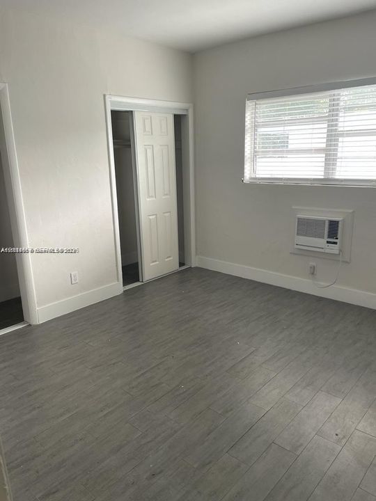 Neutral interior space featuring wood-finish flooring, a wall-mounted climate control unit, and a built-in closet with double-panel doors