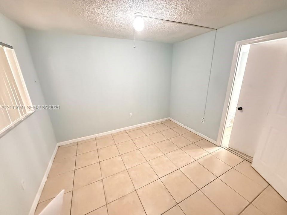 Interior room featuring neutral-toned tile flooring, light-colored wall finish, window with vertical blinds, and a single-bulb ceiling fixture