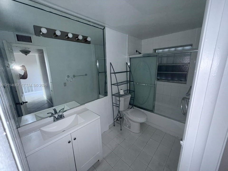 Bathroom featuring a vanity with a white basin, a full-width wall mirror, a five-light fixture, and a tub-shower combination with sliding glass doors