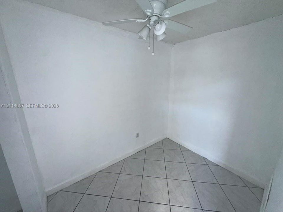 Neutral interior space featuring white walls, diagonal-set ceramic floor tiles, and a white ceiling fan with integrated lighting