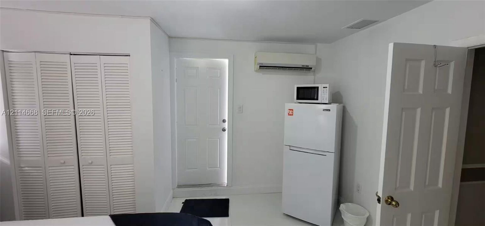 Double louvered-door closet, wall-mounted ductless air conditioning unit, solid-core six-panel door, and white appliance suite featuring a top-freezer refrigerator with microwave