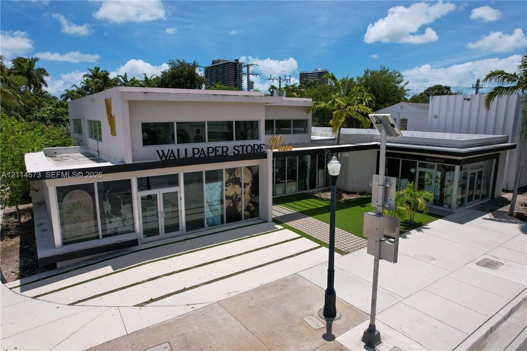 Commercial building featuring a flat-roof architectural design, expansive glass storefront windows, a paved walkway, and synthetic turf area