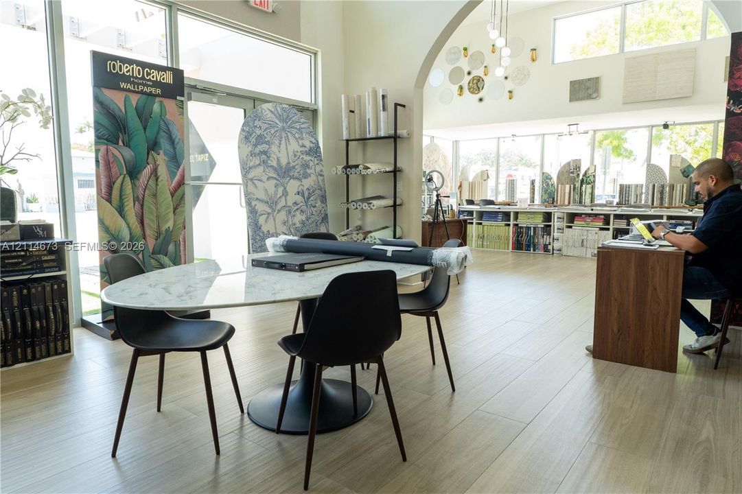 Open-concept commercial space featuring expansive floor-to-ceiling glass storefront windows, light-toned wood-finish flooring, a prominent architectural archway, and recessed ceiling lighting