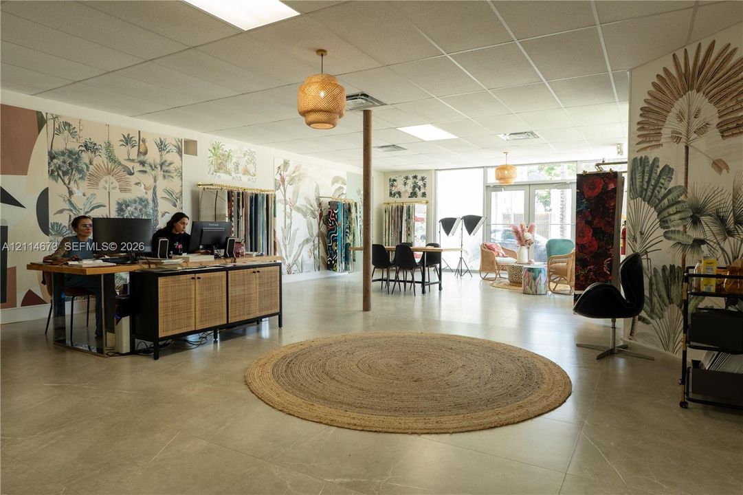 Open-concept interior featuring large-format tile flooring, textured wallpaper accents, drop-down woven pendant lighting, and floor-to-ceiling glass panel windows