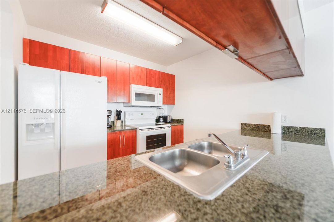 Kitchen featuring stone-finish countertops, stainless steel double-basin sink with a chrome faucet, wood-finish cabinetry, and built-in appliances including a refrigerator, microwave, and range