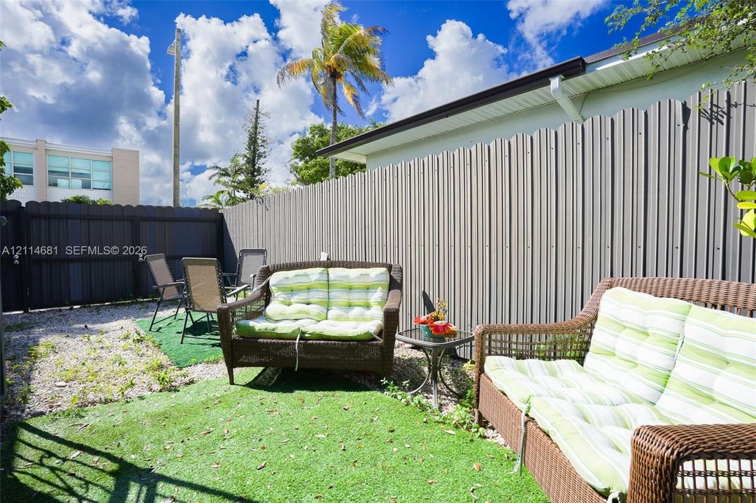 Enclosed outdoor patio space featuring corrugated metal privacy fencing and synthetic turf ground covering
