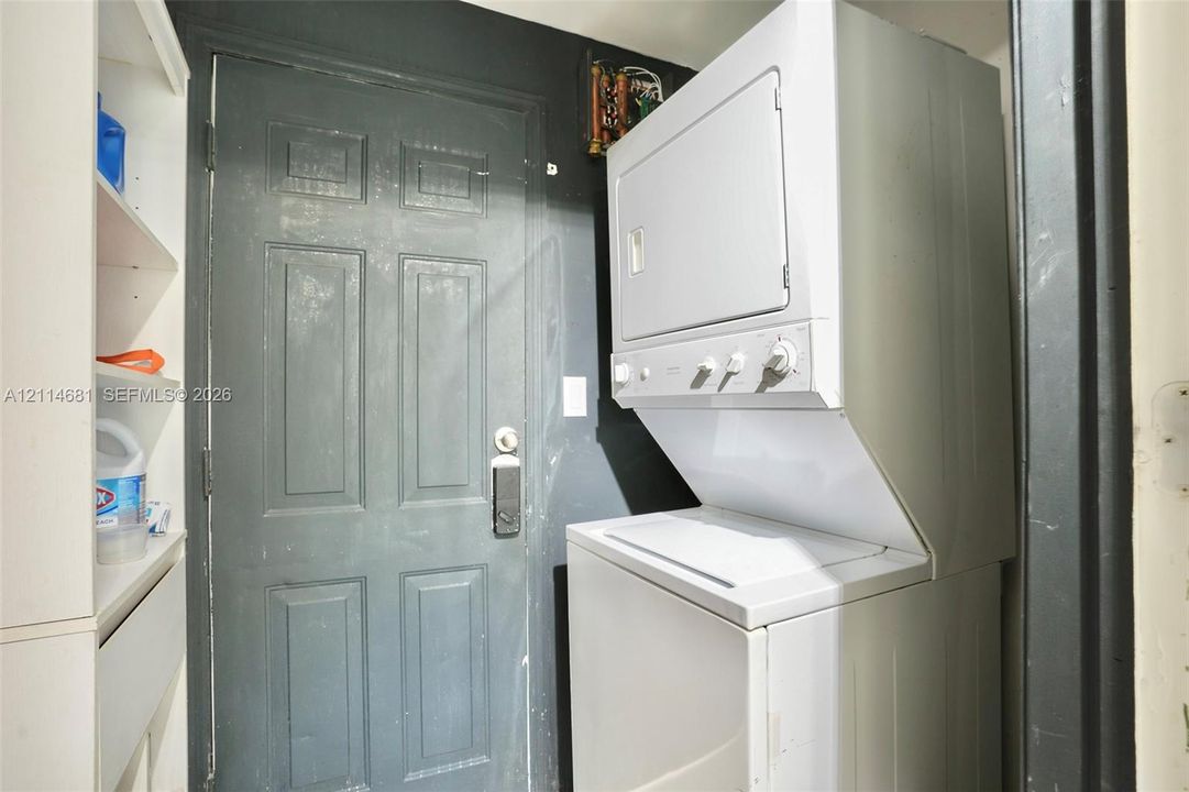 Stacked laundry unit with white finish, built-in shelving, and paneled entry door