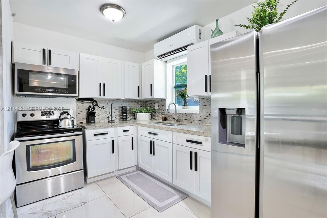 Kitchen featuring white shaker-style cabinetry with matte black hardware, stone-finish countertops, stainless steel appliances, a mosaic tile backsplash, and polished tile flooring