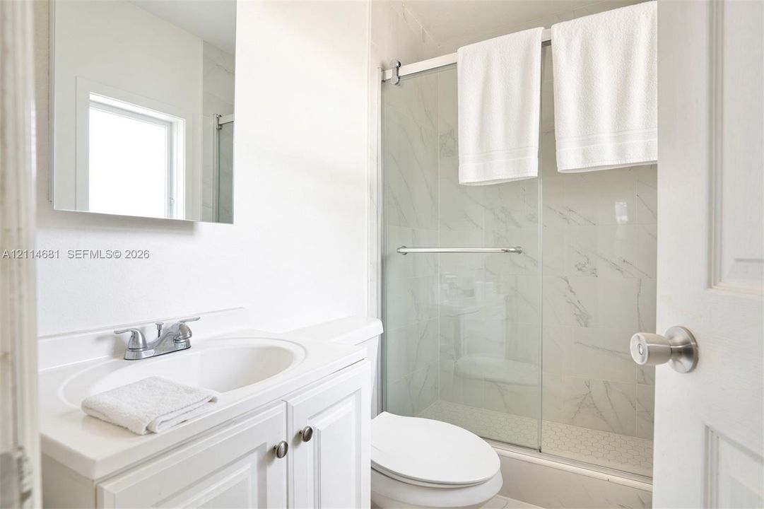 Bathroom featuring a white vanity with an integrated sink, polished chrome dual-handle faucet, wall-mounted mirror, and a shower enclosure with glass sliding doors and stone-patterned wall tile