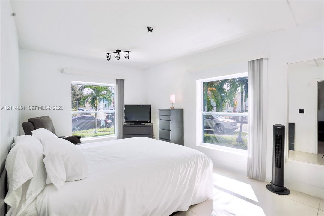 Neutral interior featuring large windows with natural light, tiled flooring, track lighting, and a mirrored wall panel
